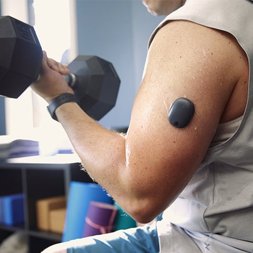 Uomo che solleva pesi mentre indossa un CGM a lungo termine per il diabete.