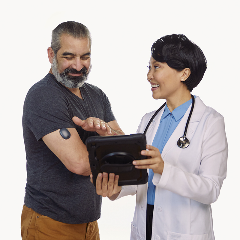 Un professionnel de santé montre à un patient comment suivre les valeurs du glucose d’un CGM implantable sur une tablette.