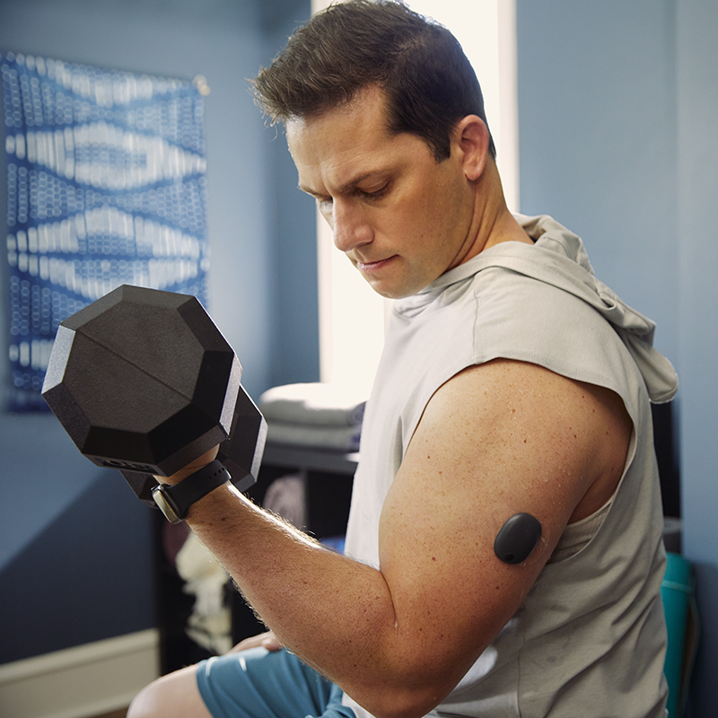 Un homme avec un système CGM sur son bras levant des poids en salle de sport.