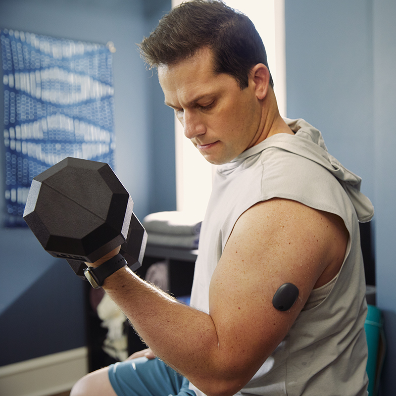 Uomo che solleva pesi in palestra mentre indossa un sistema CGM sul braccio.