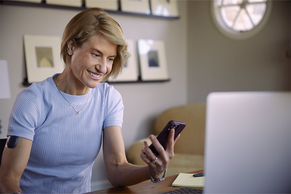 Une femme utilisant son téléphone pour rechercher des informations sur la couverture d’assurance pour un CGM implantable.