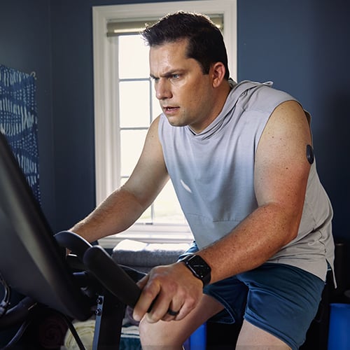 Uomo che pedala su una cyclette mentre indossa un CGM Eversense.