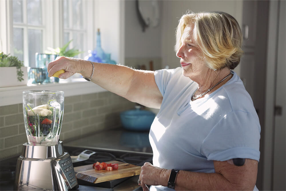 Une femme préparant un smoothie tout en portant un appareil de surveillance du glucose en continu.
