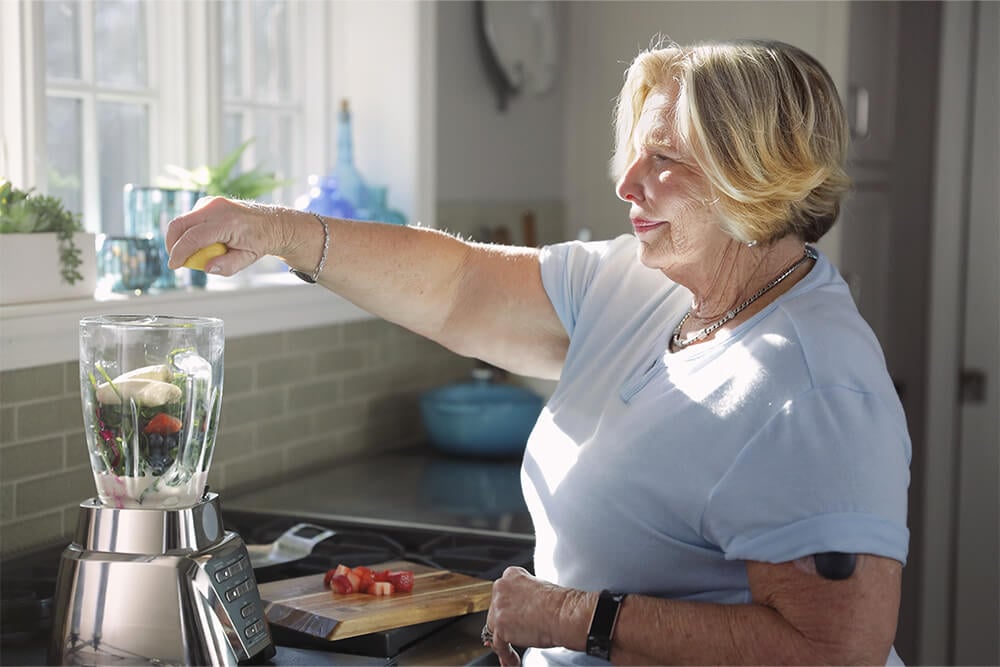 Frau mit kontinuierlichem Glukosemessgerät mixt einen Smoothie