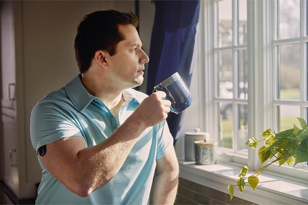 Un homme regardant par la fenêtre tout en portant un dispositif de CGM.