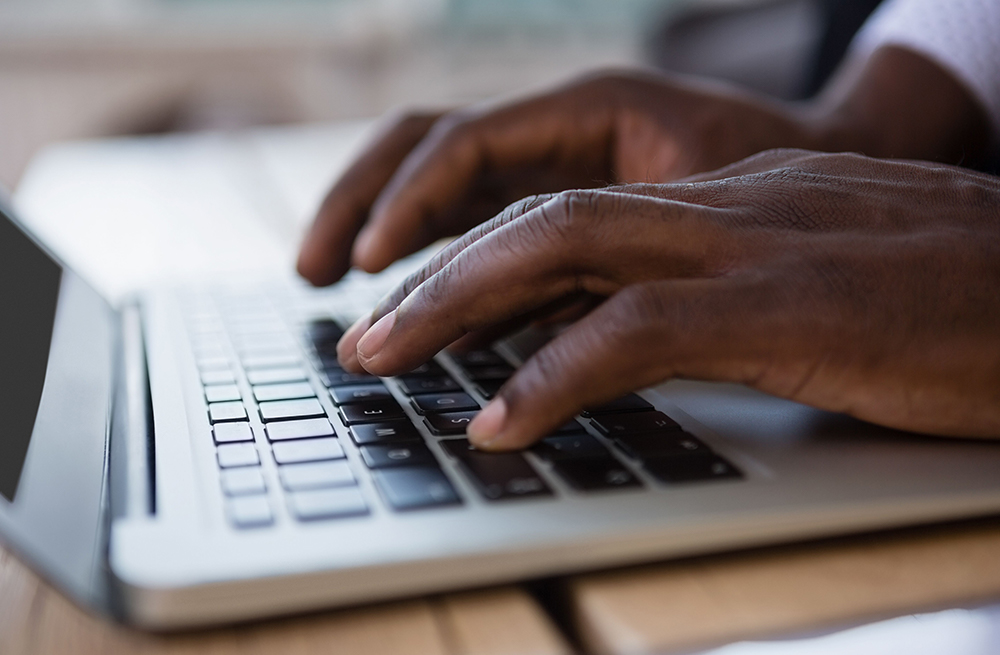 Un homme tapant sur un ordinateur pour trouver des informations sur les dispositifs de CGM, notamment sur leur fonctionnement.