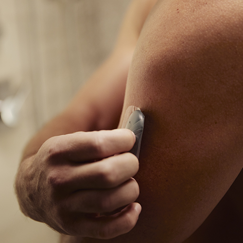 Un homme retirant un système de surveillance du glucose de son bras avec un transmetteur du CGM.