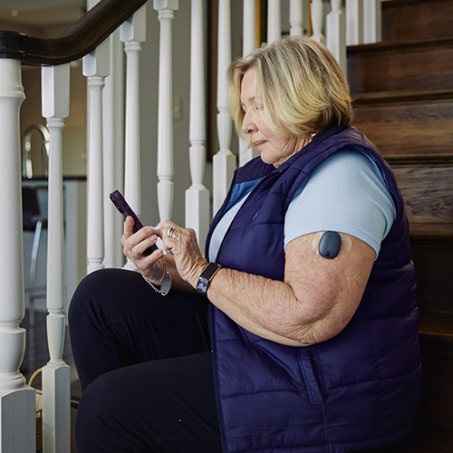 Frau sitzt auf Treppe und verwendet die Eversense CGM App mit ihrem implantierbaren CGM
